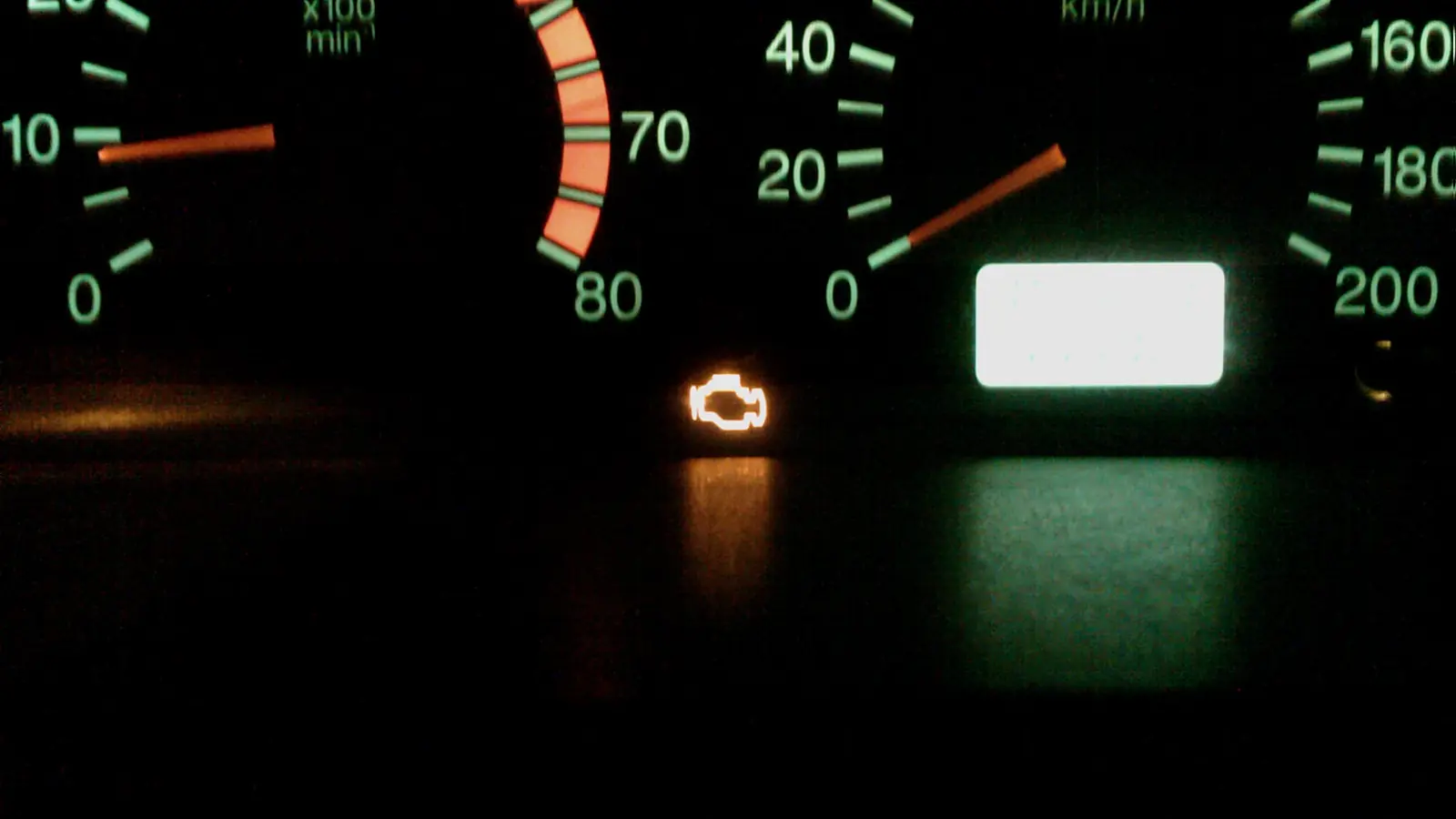 An amber check engine light lit on a car instrument cluster at night
