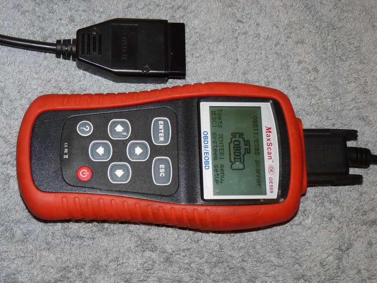 A handheld OBD-II scan tool with its cable and 16-pin diagnostic connector, the same kind of plug a smog check station uses to read the car's computer