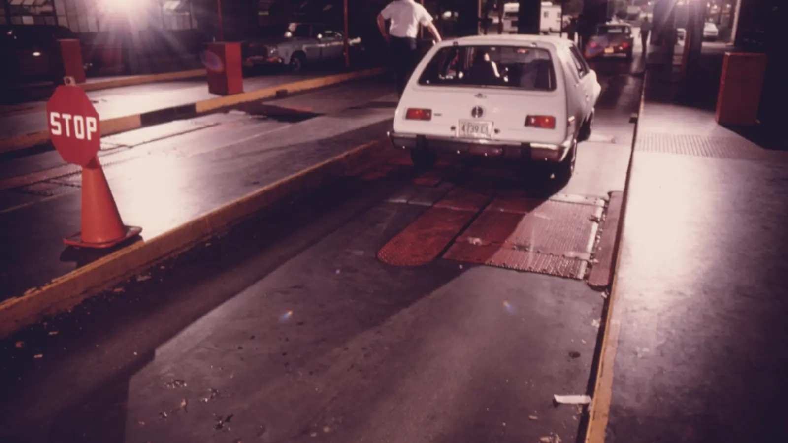 A car rolls out of an emissions inspection lane past a stop sign and traffic cone
